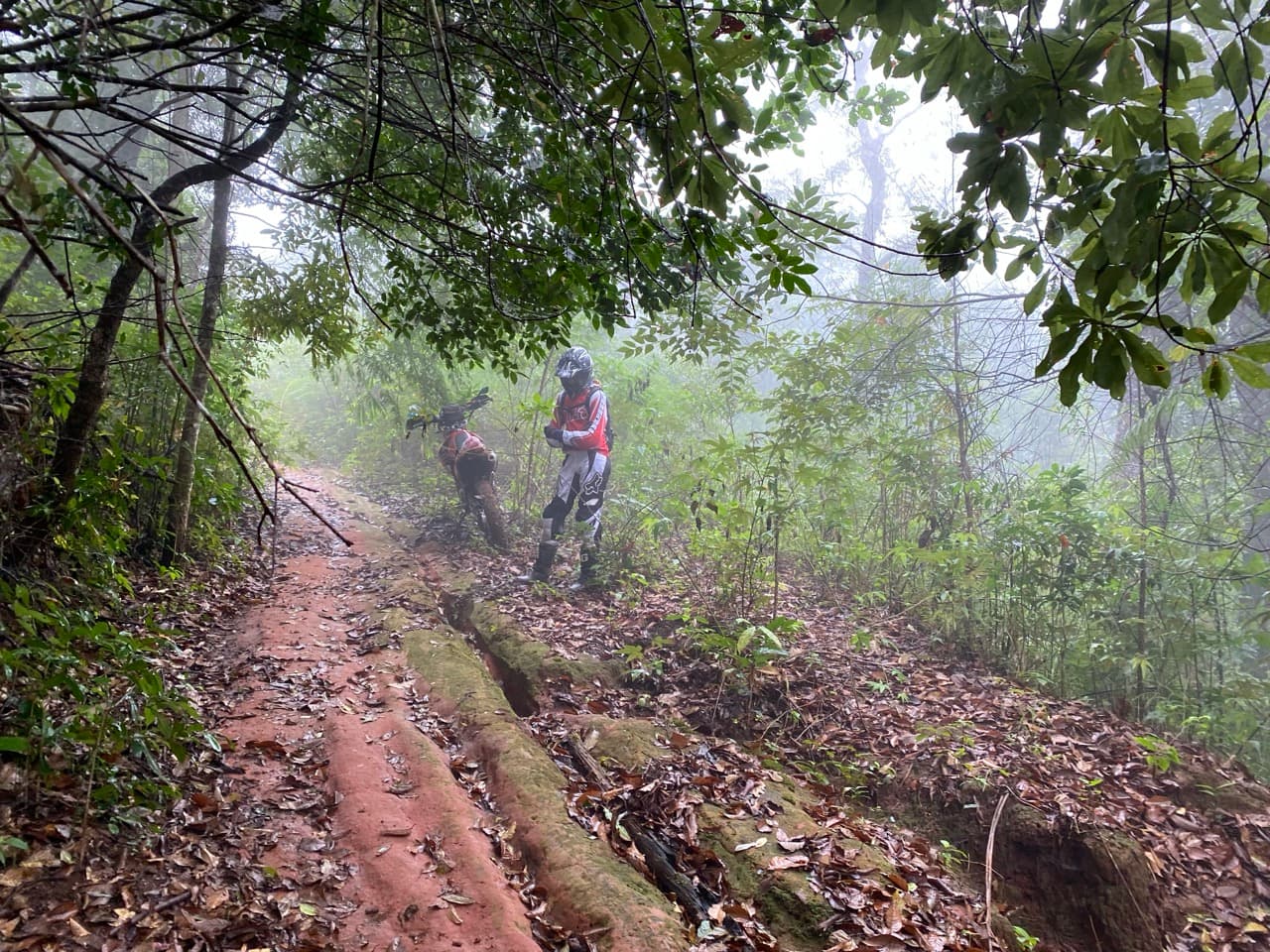 Northern Thailand terrain — red clay double-track, rooted jungle single track, and river crossings within the same day